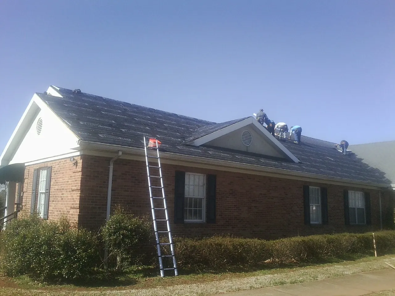 Crew tearing shingles off a brick ranch roof with a ladder set — Metal Roof Repair work by our crew in Johnson City