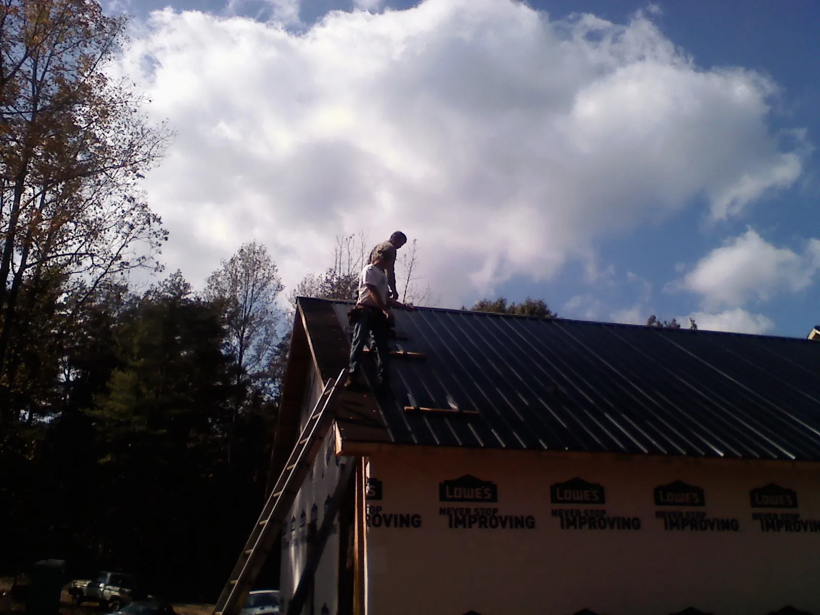 Roofer fastening dark metal panels high against a cloudy sky, from a Roof Inspection job in Johnson City