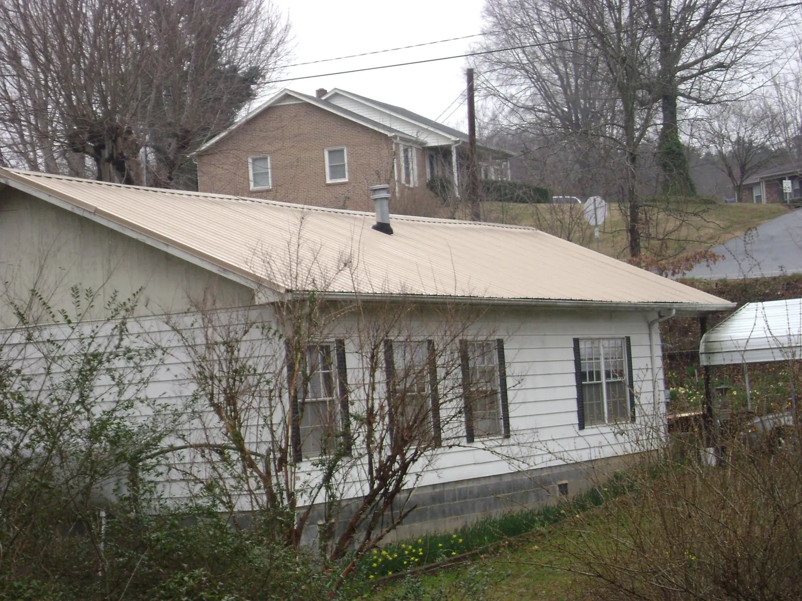 Tan metal roof on a white sided house set into a hillside — Commercial Roofing by Roofing Brothers in Johnson City
