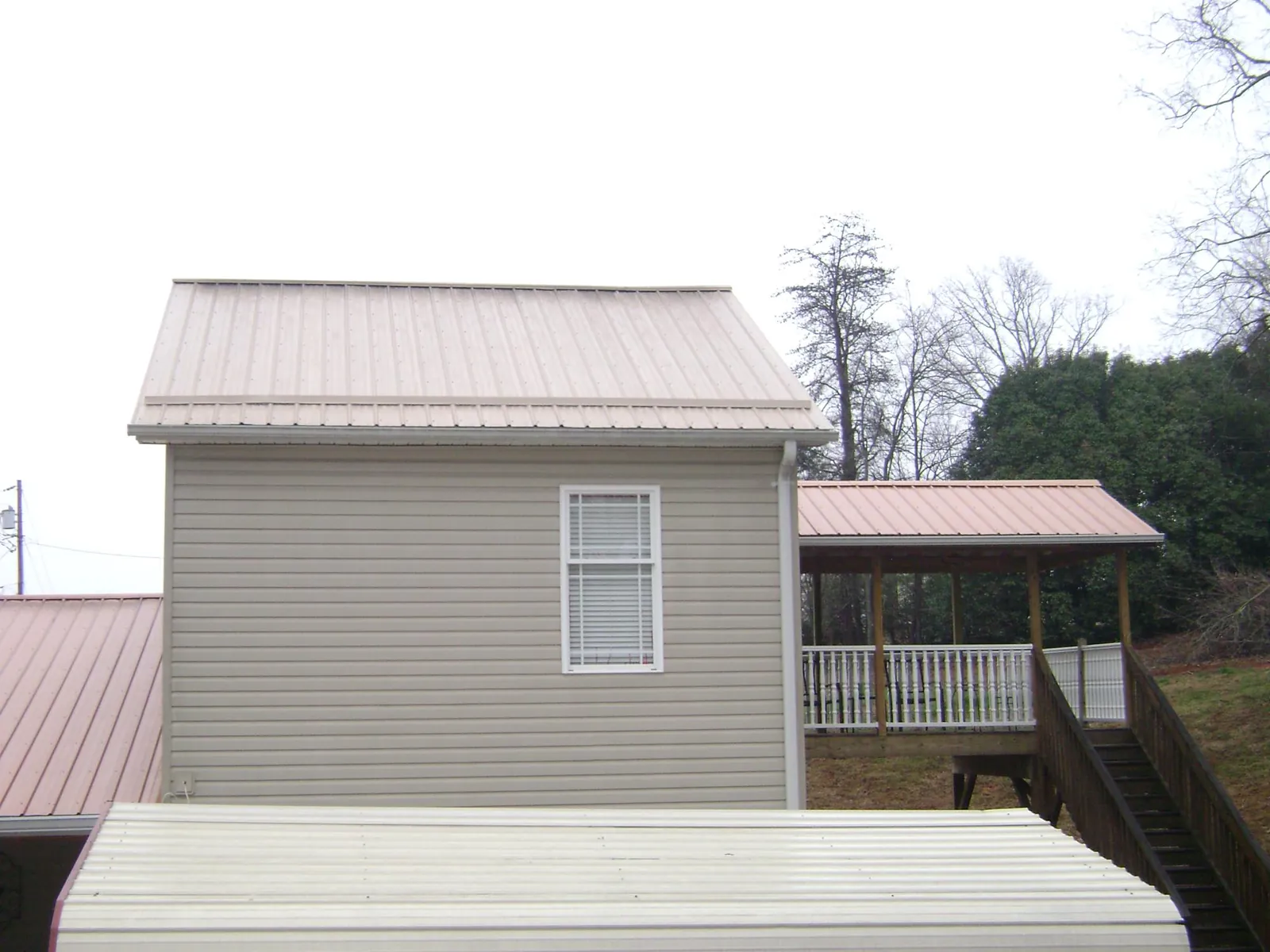 Tan metal roofs on a two story addition and attached porch, from a Roof Replacement job in Johnson City
